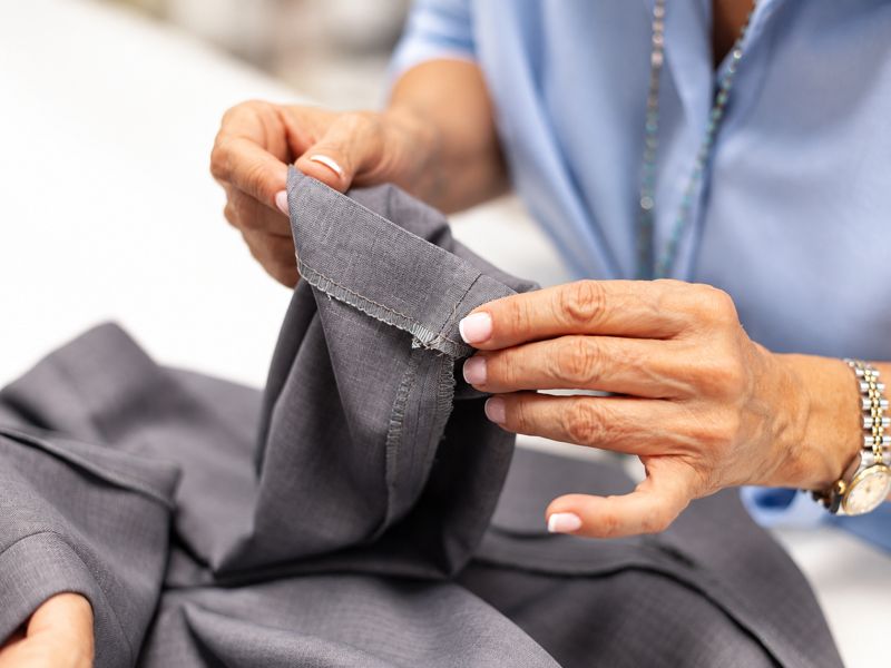 Unas manos revisan la costura de una prenda gris